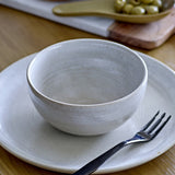 Taupe Stoneware Bowl 13cm in speckled grey ceramic, shown on a matching plate with a fork, set on a wooden table beside olives.