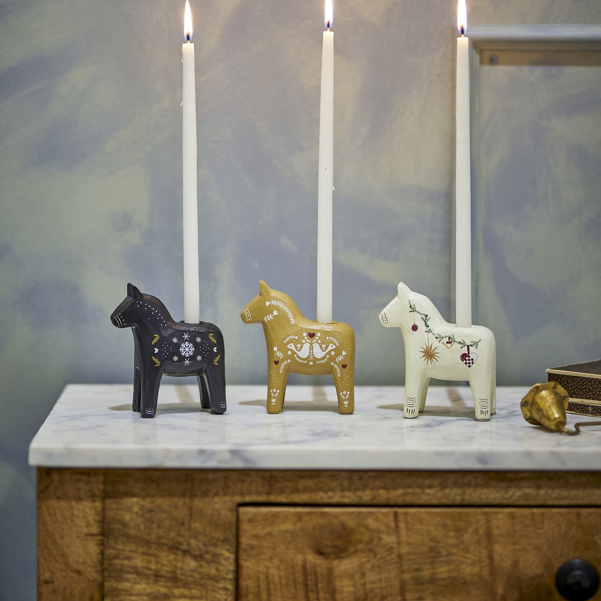 Set of three Siffer resin horse candle holders in black, gold, and white with folk-art motifs, each holding a tall white taper candle on a marble-topped sideboard.