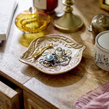 Lizz Floral Stoneware Bowl 18x16cm in brown with raised floral and leaf motif, leaf-shaped edges, shown on a wooden table holding jewellery among decorative objects.