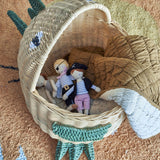 Eddi Dinosaur Rattan Basket in natural, shown open with pirate dolls and a mustard quilted blanket inside, woven spines and green clawed feet visible against a patterned rug.