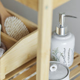 Bea Crackle Stoneware Soap Dispenser in beige with chrome pump top and floral motif, shown on a wooden bathroom shelf beside a matching lidded jar.