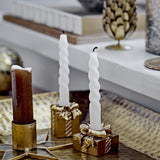 White Twist Candles, slim spiral paraffin tapers, shown lit in gold gift-box candle holders beside a brown pillar candle on a decorative tray.