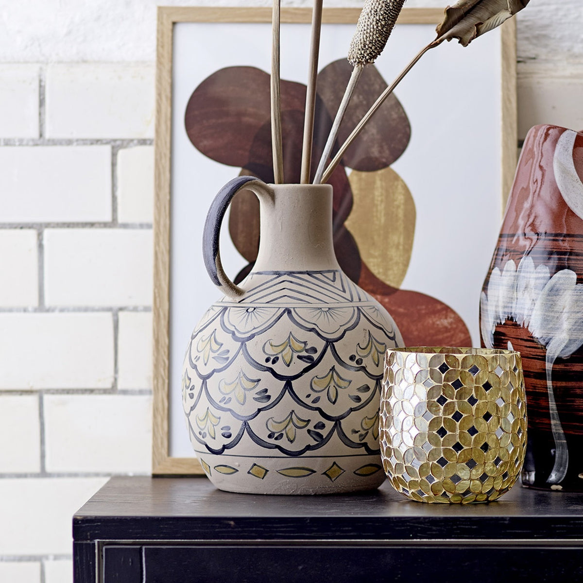 Beige Nadya round stoneware vase, 27cm, with loop handle and hand-painted chevron, fan and scallop patterns, styled with dried stems and a candle holder.
