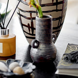 Casaya Stoneware Vase 13.5cm in brown with ringed handles and a textured, ridged body, displayed on a dark table beside a patterned ceramic vase and books.