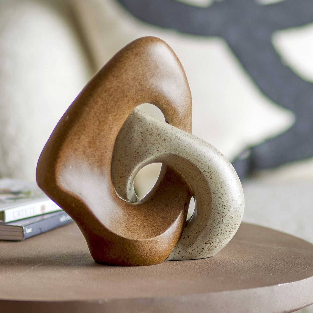 Esad Resin Ornament in Brown, a sculpted interlocking loop figurine in brown and speckled cream resin, displayed on a side table in a living room setting.