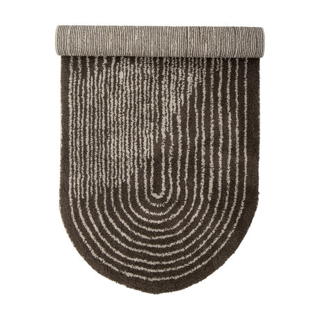 Zhina Oval Cotton Rug 160x70cm in Brown, shown rolled to reveal striped grey backing above a tufted shaggy pile with concentric oval lines, on a plain white background.
