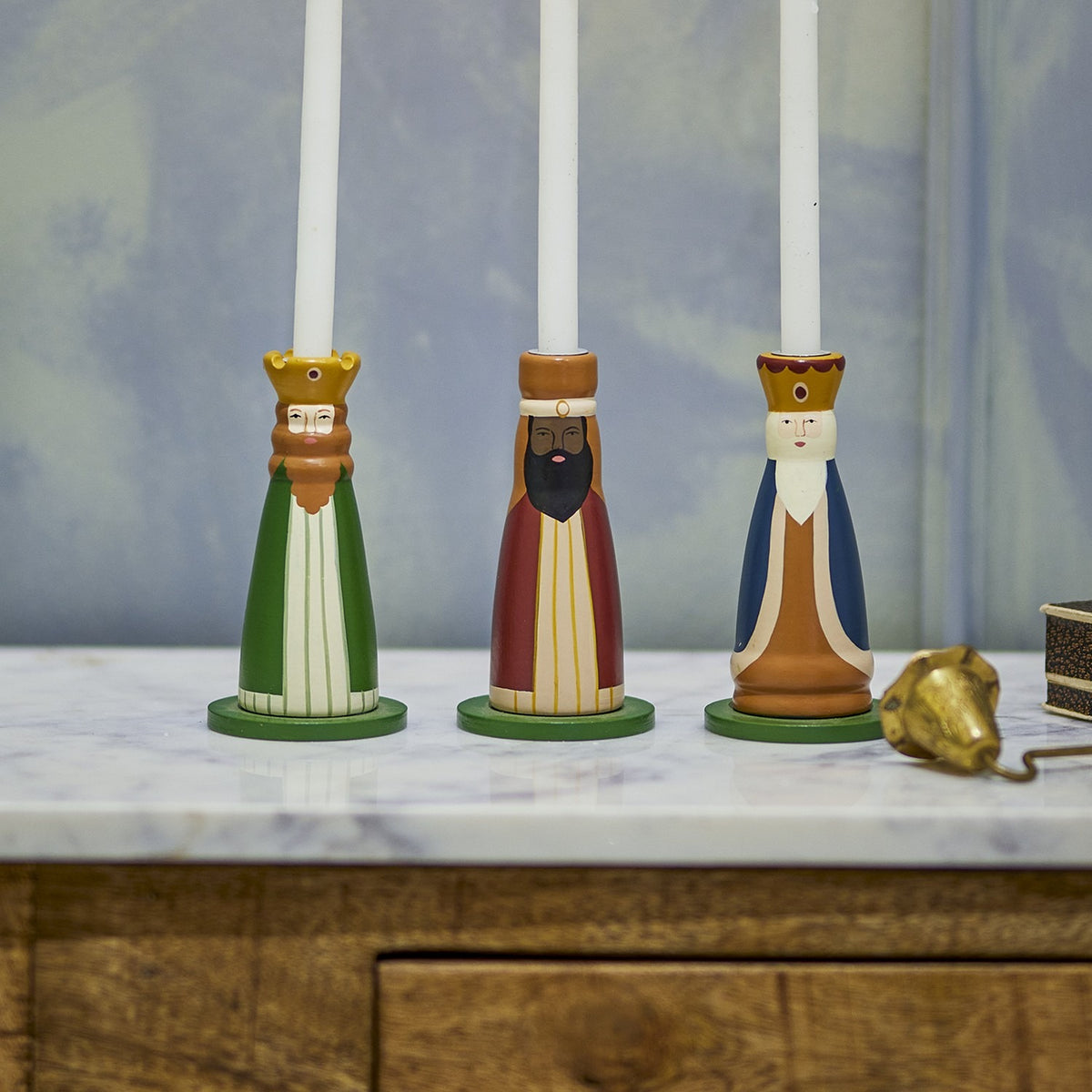 Betiel wooden Christmas candle holders, set of three bearded king figures in green, red and blue robes with crowns, holding white taper candles on a marble surface.