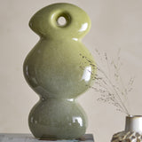 Kaui Stoneware Ornament in green, a sculptural stack of rounded ceramic forms with a pierced oval head, glossy speckled glaze shading from light to deep green, set against a neutral background.