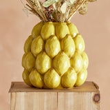 Limone Stoneware Vase 22cm in yellow, moulded as clustered glossy lemons with a narrow round opening, holding dried flower stems on a wooden block against a peach background.