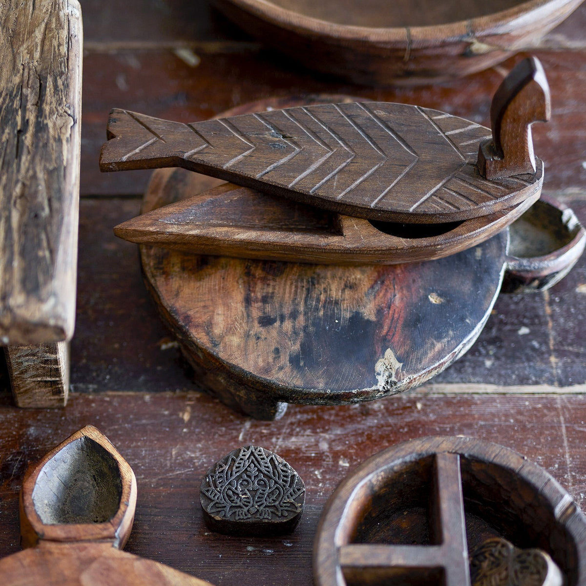 Hamida fish-shaped wooden storage box with lid, brown reclaimed wood with chevron scale carving, shown open among other carved wooden decor pieces.