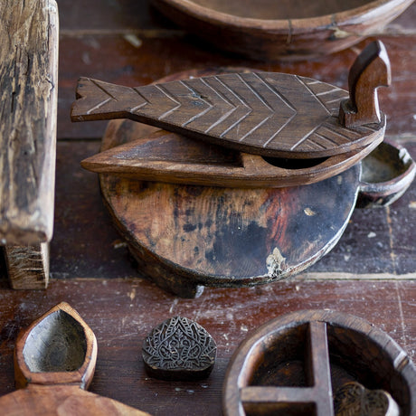 Hamida fish-shaped wooden storage box with lid, brown reclaimed wood with chevron scale carving, shown open among other carved wooden decor pieces.