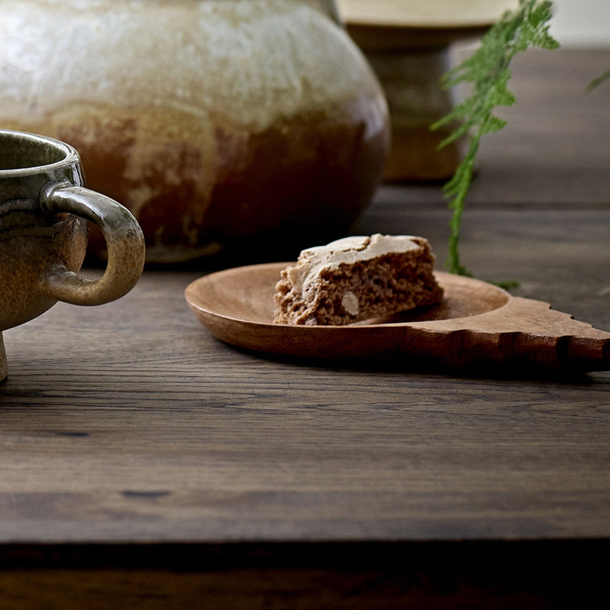 Tiara wooden acacia bowl with round dished centre and stepped tab handle, holding a slice of cake on a dark wood table beside a ceramic mug.