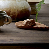 Tiara wooden acacia bowl with round dished centre and stepped tab handle, holding a slice of cake on a dark wood table beside a ceramic mug.