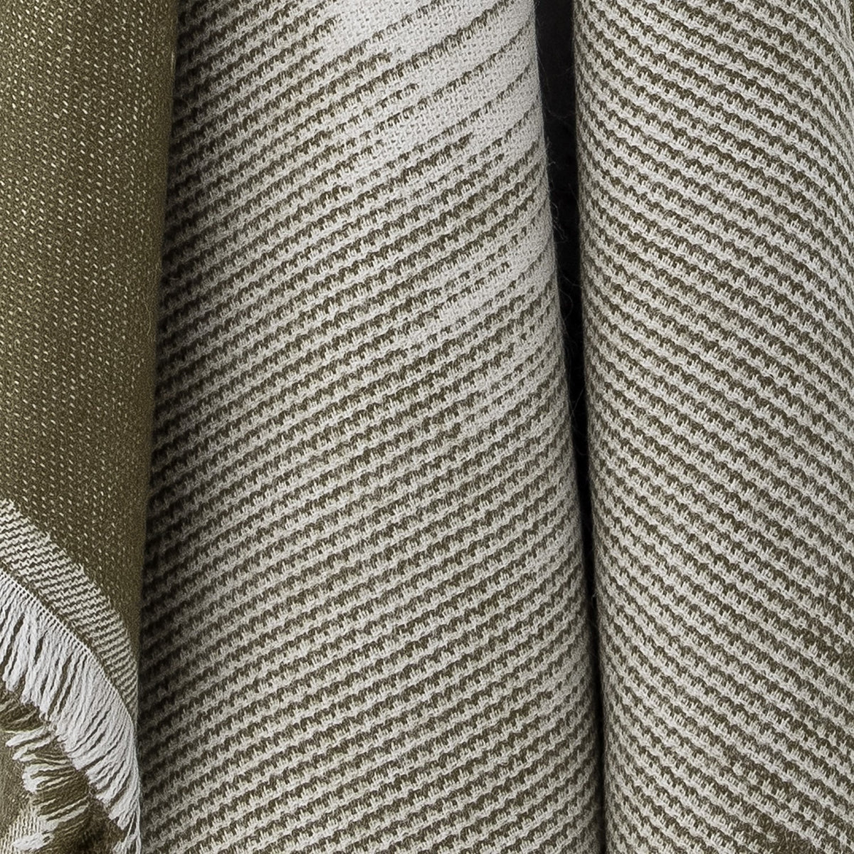 Close-up of the Lucienne Throw in green, showing a woven fabric with diagonal flecked striping transitioning from deep green to lighter tones with fringed edge detail.