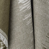 Close-up of the Lucienne Throw in green, showing a woven fabric with diagonal flecked striping transitioning from deep green to lighter tones with fringed edge detail.