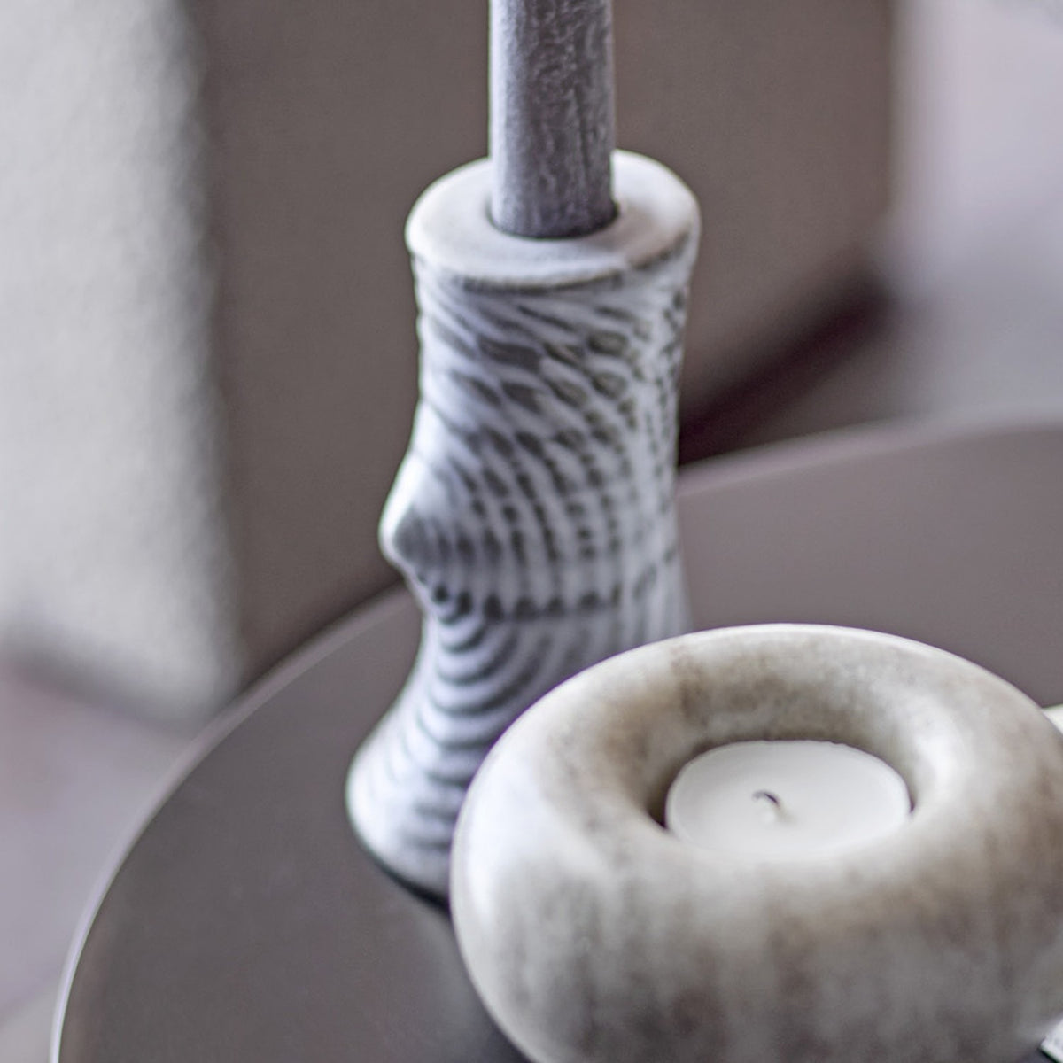 Raheem Stoneware Candle Holder 13cm in grey, taper-style with ridged, branch-like texture, shown beside a round tealight holder on a dark tabletop.