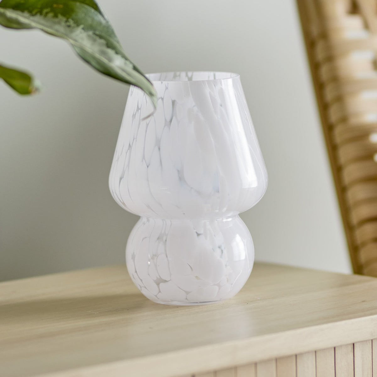Halim Mushroom Glass Vase 18.5cm in White, with a flared bowl and rounded base in marbled white glass, shown on a wooden surface with a trailing green leaf.