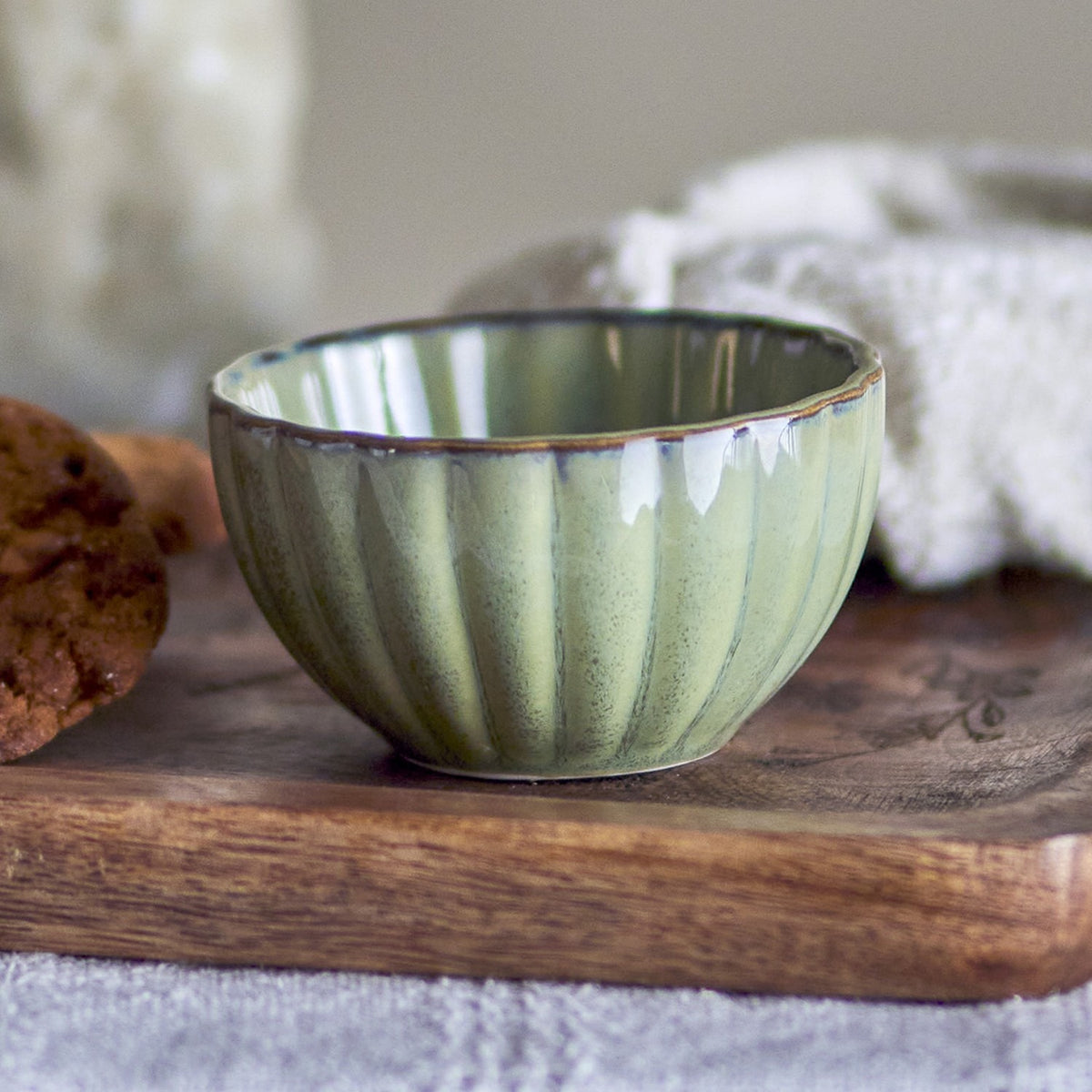 Latina Stoneware Bowl 12cm in Green with fluted sides and a wavy rim, shown on a wooden board beside a biscuit and cloth.
