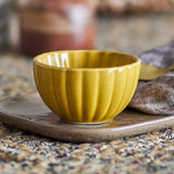 Latina Stoneware Bowl 12cm in yellow, round fluted design with ribbed sides and glossy glaze, shown on a stoneware plate beside a cloth napkin.