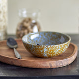 Paula Mottled Stoneware Bowl 16cm in brown and blue reactive glaze, shown on a wooden tray with a spoon and jar in a kitchen setting.
