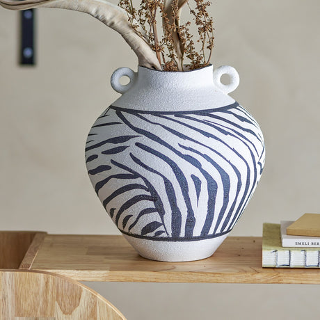Togo Striped Stoneware Vase 26cm in White with bold zebra-stripe pattern and loop handles, shown on a wooden shelf holding dried foliage.