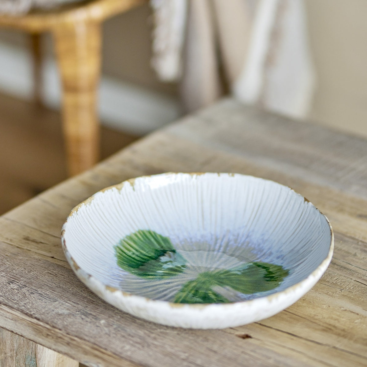 Mati Fluted Stoneware Bowl 29cm in White with a wavy rim, radiating fluted texture, and a painted green leaf motif, shown on a wooden table.