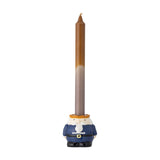 Feast Nutcracker stoneware Christmas candle holder in navy, white and orange, modelled with a bearded face and belted coat, holding a tall brown taper candle against a plain white background.