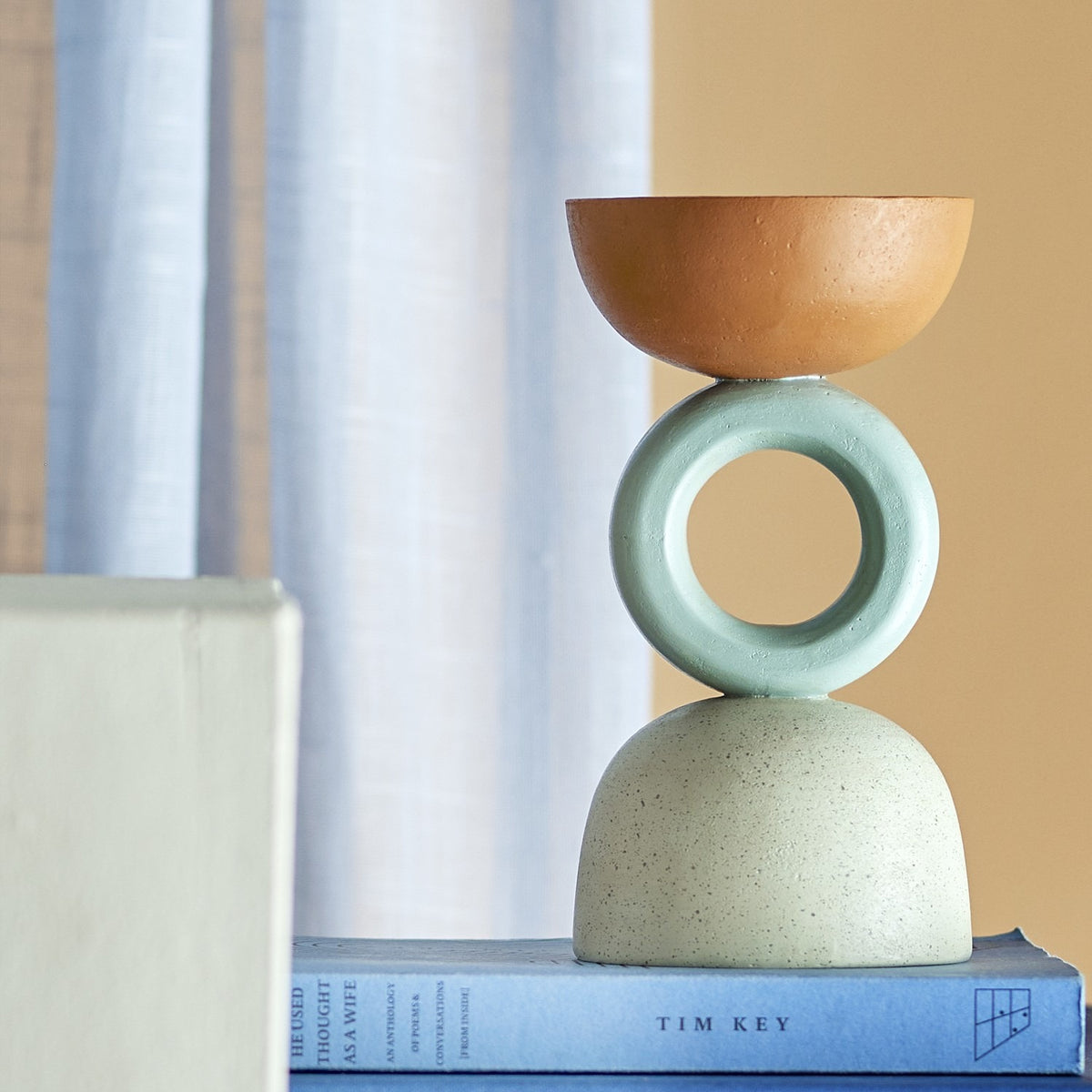 Loretta Speckled Resin Tealight Holder in terracotta and sage, stacked bowl, ring and speckled dome design, shown on books against a curtain backdrop.