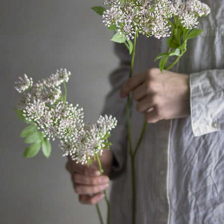 Fennel Artificial Stem in Pink held by hand, showing two lacy pink floret heads on a slender branching stem against a neutral background.