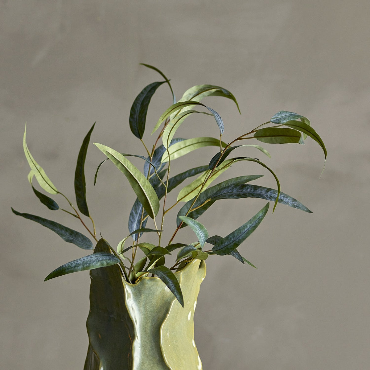 Eucalyptus Artificial Stem 101cm in Green, arranged in a green ceramic vase with narrow curving leaves in varied shades, set against a plain grey background.