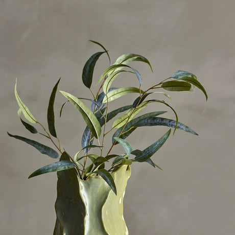 Eucalyptus Artificial Stem 101cm in Green, arranged in a green ceramic vase with narrow curving leaves in varied shades, set against a plain grey background.
