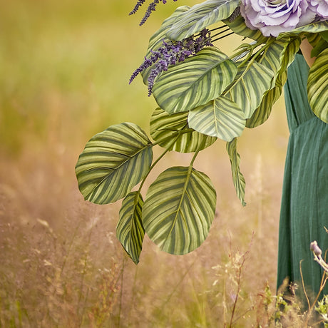 Zebra Artificial Stem in green with striped, rounded leaves, shown outdoors arranged with lavender stems and a purple bloom against a grassy field.