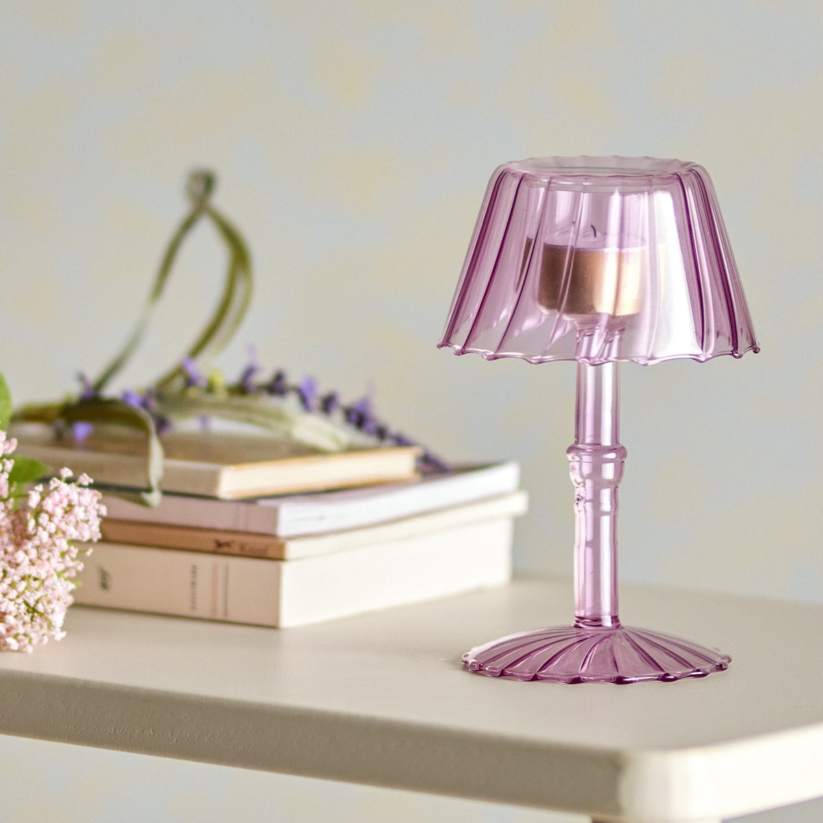 Cisco Glass Tealight Holder 18cm in pink, shaped like a table lamp with a fluted shade and ribbed stem on a scalloped foot, displayed on a shelf beside books and flowers.