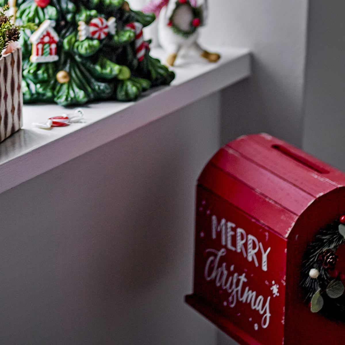 Carlo Christmas Decoration in red MDF, a postbox-style ornament with slatted curved roof, letter slot, "Merry Christmas" script, and a small wreath, displayed near a festive mantel.