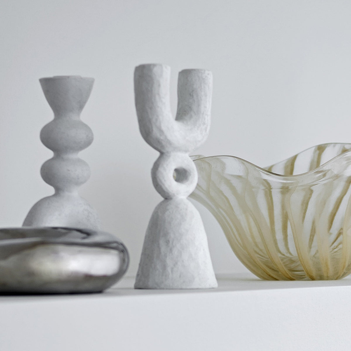 Syra Resin Candle Holder 22cm in White, a U-shaped twin candle holder with a ring link and flared bell base, shown with a ribbed candle holder and glass bowl.
