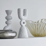 Syra Resin Candle Holder 22cm in White, a U-shaped twin candle holder with a ring link and flared bell base, shown with a ribbed candle holder and glass bowl.
