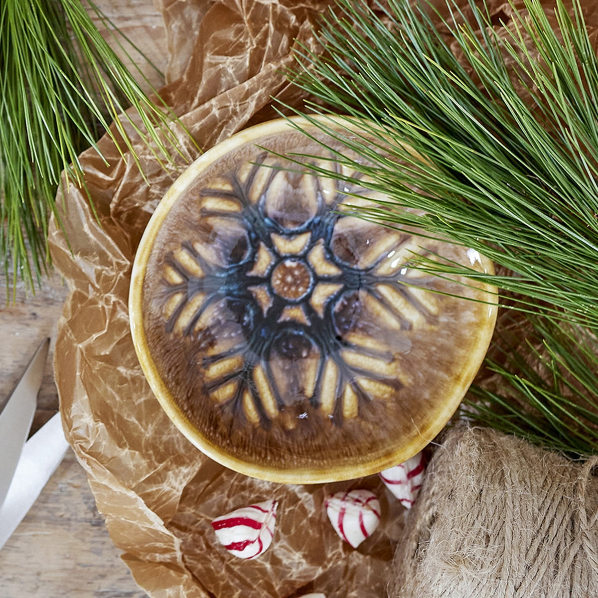 Acco Stoneware Christmas Bowl 12cm in brown, showing a wavy rim and radiating frost-like motif in reactive glaze, styled with pine branches and candy decorations.