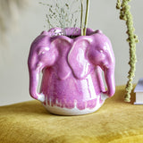Pontus Stoneware Vase 15.5cm in Pink, ceramic with a ring of elephant heads, drip-glazed finish, shown with dried foliage on a mustard fabric surface.