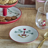 Yule Stoneware Christmas Plate, cream with red rim, featuring a painted pine sprig, heart and gold horn design, shown on a table with cookies and a glass.