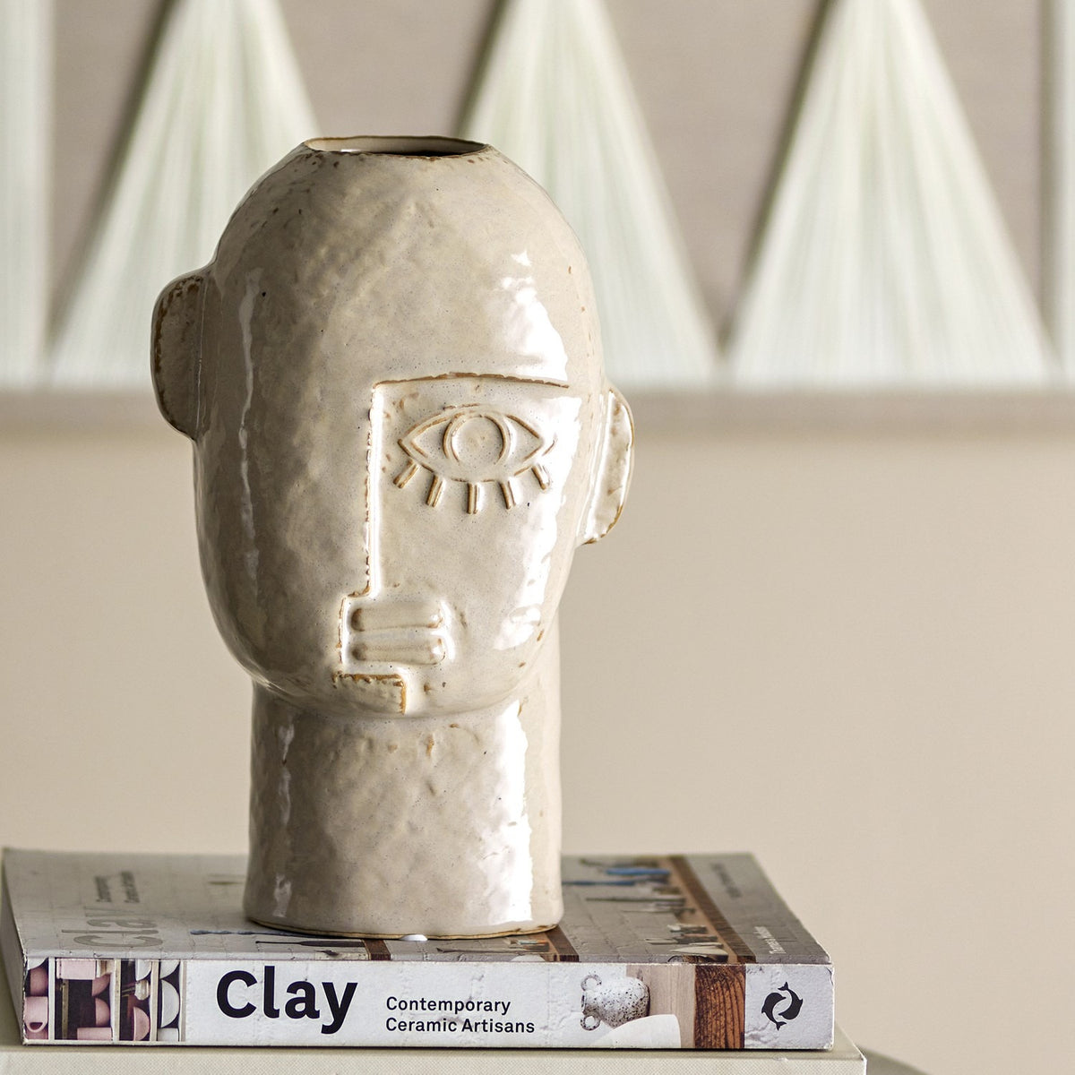 Lizzie Stoneware Vase 25.5cm in beige, head-shaped with small ears, raised single eye and face lines, glossy ceramic finish, displayed on books indoors.