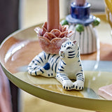 Rory Striped Stoneware Candle Holder in Multi, a white and navy ceramic tiger with a flower-shaped candle cup on its back, shown holding a pink candle on a glossy tray.