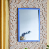 Atle Wall Mirror 40x60cm in Blue, a rectangular MDF-framed mirror mounted on a textured beige leaf-patterned wall panel beside a gold curtain.
