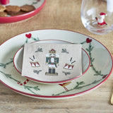Beige paper napkin from the Jolly Christmas pack of 20, printed with a nutcracker soldier and drums design, folded on a festive plate setting.