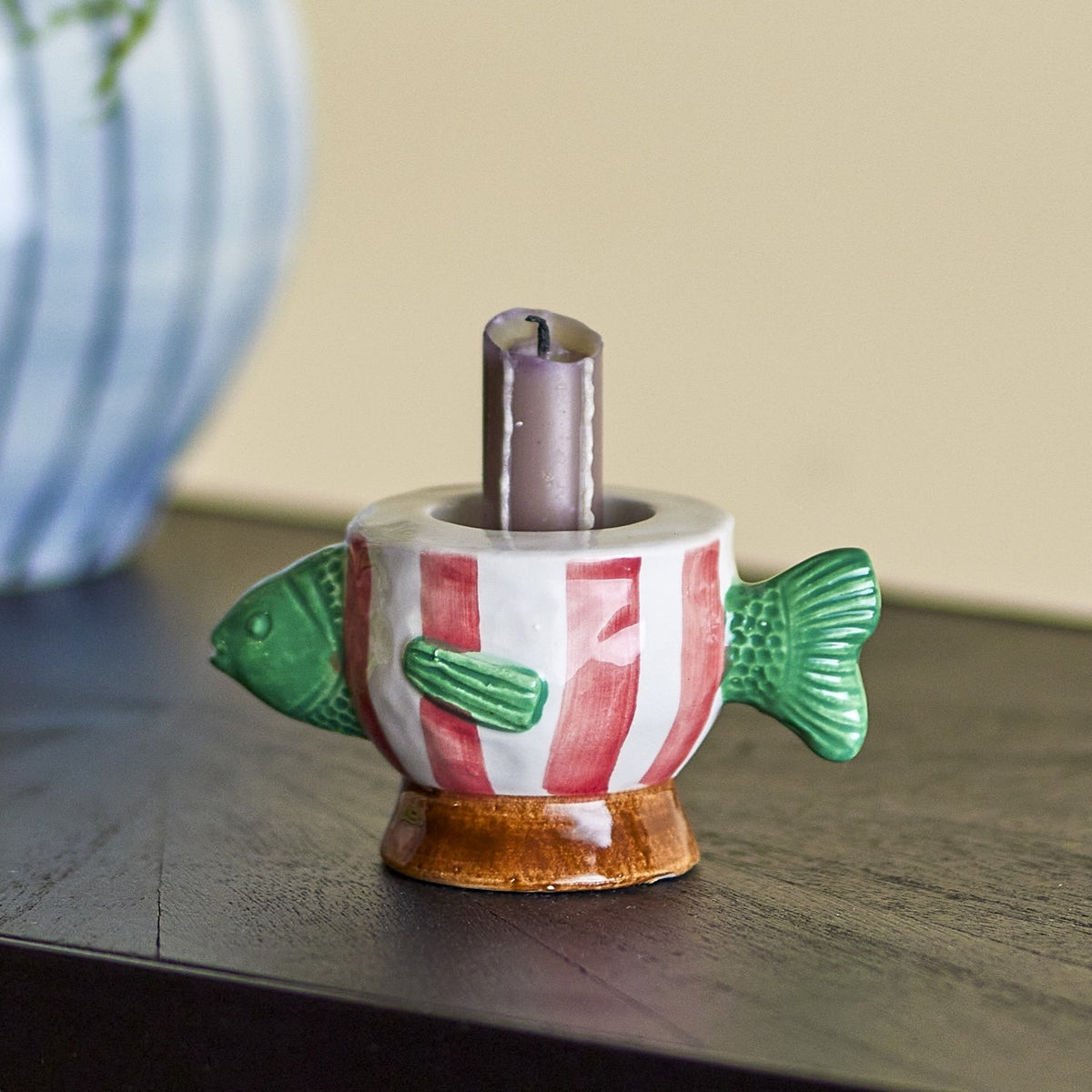 Codia Fish Stoneware Candle Holder in multicoloured ceramic, shaped like a fish with green fins and red-striped body, holding a lit candle on a tabletop.