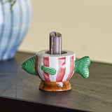 Codia Fish Stoneware Candle Holder in multicoloured ceramic, shaped like a fish with green fins and red-striped body, holding a lit candle on a tabletop.