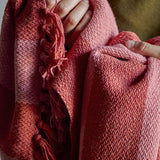 Frello Striped Cotton Throw in Orange, woven with broad two-tone stripes and knotted fringe, shown draped and held in close-up to reveal the textured cotton weave.