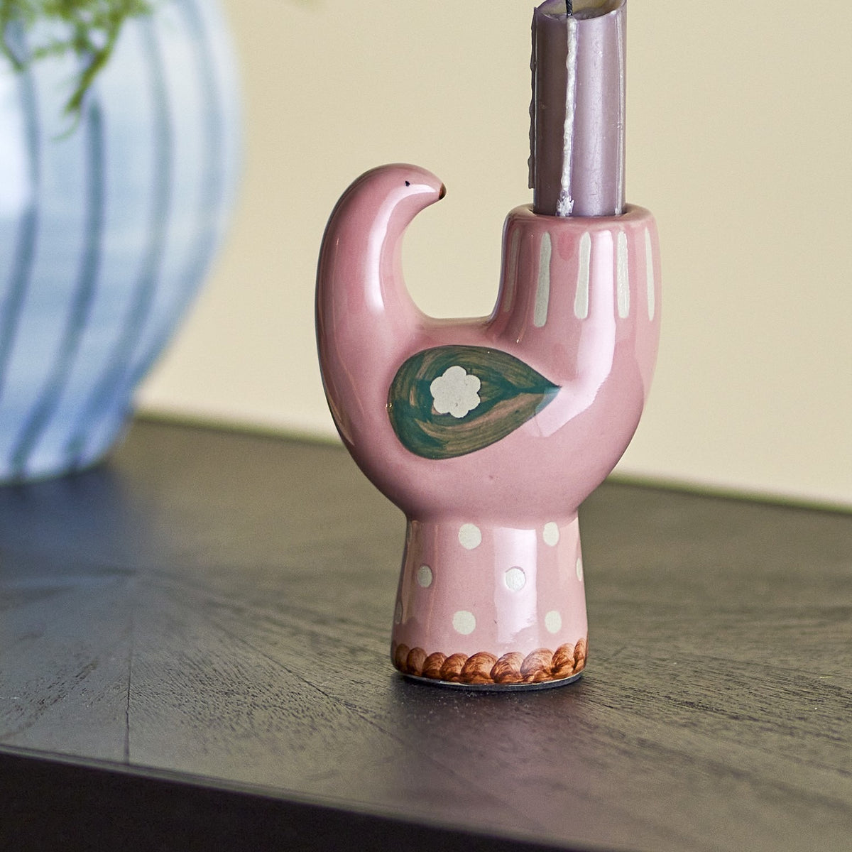 Trudy Bird Stoneware Candle Holder in pink, a stylised bird shape with curved head, green and white leaf motif, polka-dot foot, holding a taper candle on a dark surface.