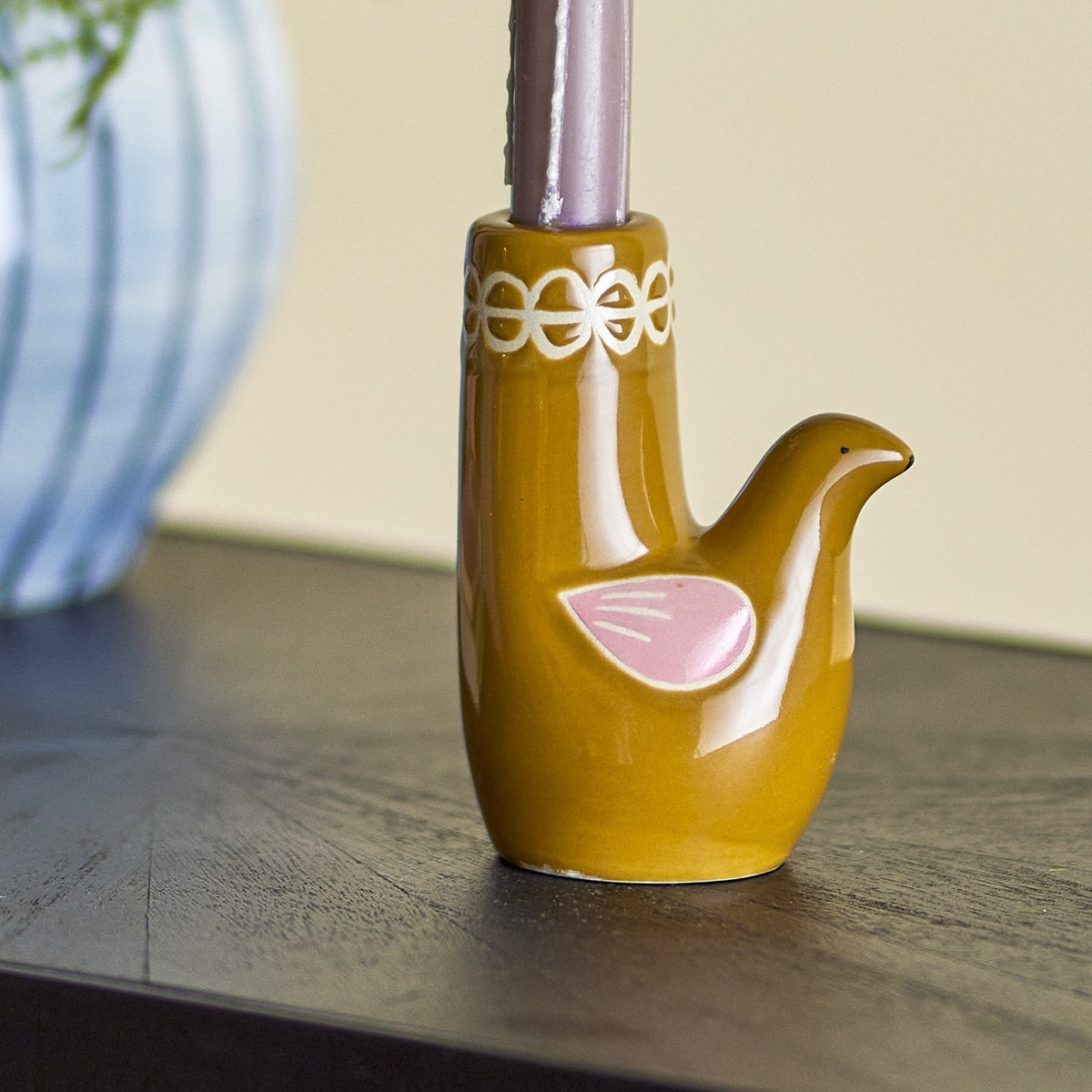 Trudy Bird Stoneware Candle Holder in glossy brown with a pink painted wing and white loop rim, holding a taper candle on a dark wood surface.
