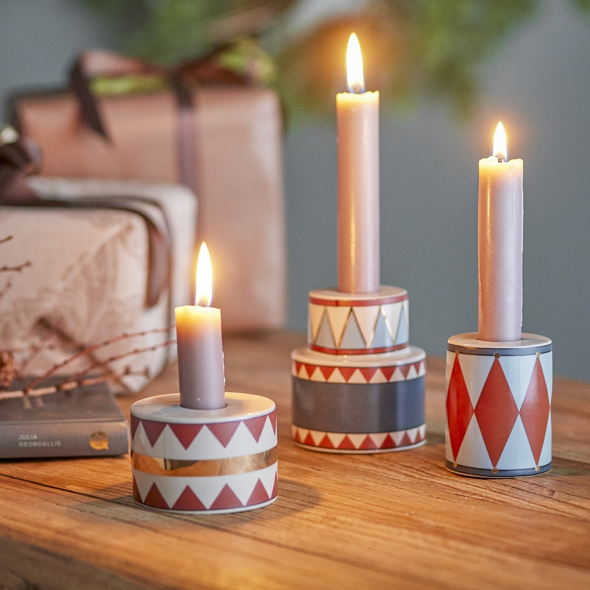 Bitja Geometric Christmas Candle Holders, set of three stoneware pieces in multicoloured zigzag, triangle, and diamond patterns, shown lit with taper candles on a wooden table.