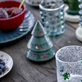 Yule Stoneware Christmas Decoration tiered tree figurine in green with painted ornament details, shown on a wooden table among glassware and dishes.
